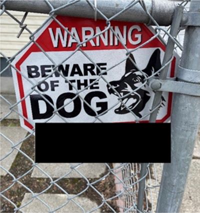 Red and white “Warning: Beware of the Dog” sign with a dog illustration mounted on a chain-link fence
